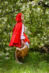 Smiling blond girl posing in a dress of little red riding hood near green trees