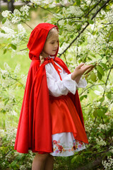 Smiling blond girl posing in a dress of little red riding hood near green trees
