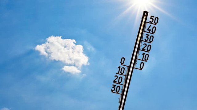 Thermometer mit strahlender Sonne, blauem Himmel und Wolken im Hintergrund
