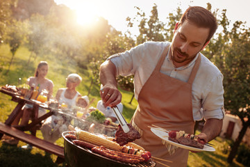 Family grilling meat on a barbecue - obrazy, fototapety, plakaty