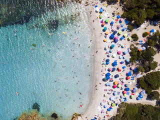 Fototapeta na wymiar View from above, aerial view of an emerald and transparent Mediterranean sea with a white beach full of colored beach umbrellas and tourists who relax and swim. Costa Smeralda, Sardinia, Italy.