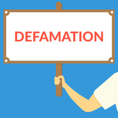 DEFAMATION. Hand holding wooden sign