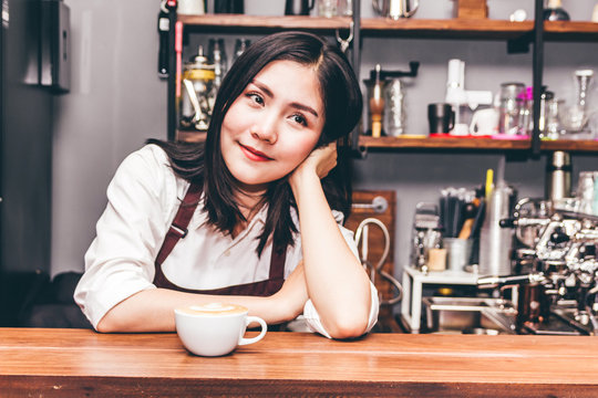 Portrait of woman barista small business owner smiling behind the counter bar with cup of coffee in a cafe