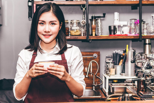 Portrait of woman barista small business owner smiling behind the counter bar with cup of coffee in a cafe