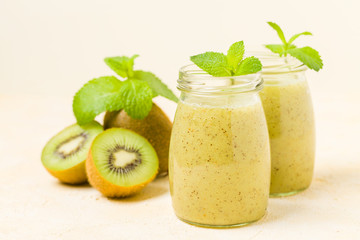 Kiwi smoothie decorated with fresh green mint leaves and raw ripe cut fruit on yellow pastel background.