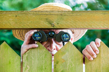 a curious neighbor stands behind a fence and watches with binoculars
 - obrazy, fototapety, plakaty