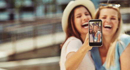 Laughing friends taking selfies together outside on sunny summer