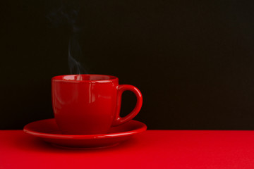 Hot tea on a black background. Tea in a red cup on a black background. Steam from hot tea on a mug.