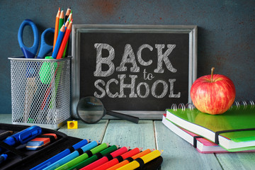 Stationery, apple and banana on a wooden table in front of blackboard with text