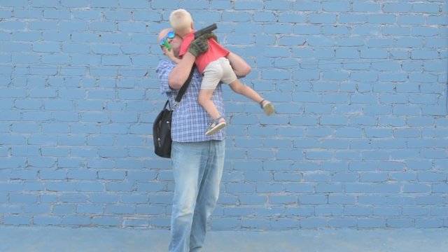 Elderly man with shaved head wearing sunglasses is holding small child and gun in his hands. boy is holding child's shovel. man shoots around at enemies. Taking care of your child's safety