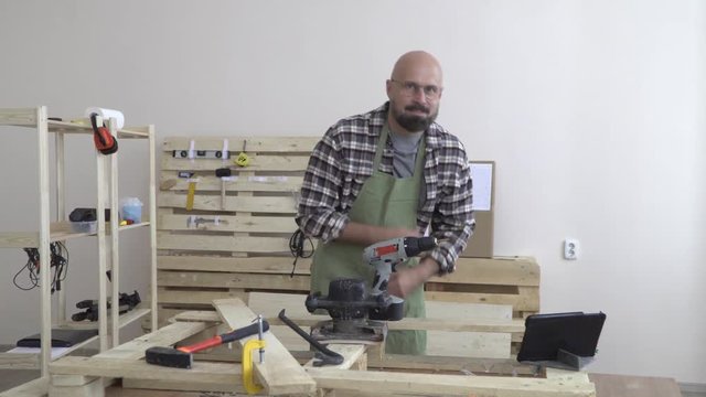 a grown 50 year old man in a plaid flannel shirt portrait of an artisan in working clothes in the Studio with the gadget on the desktop. hipster style. artisan business