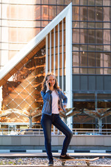 teen girl standing on a skateboard and talking on a mobile phone. City landscape of skyscrapers.