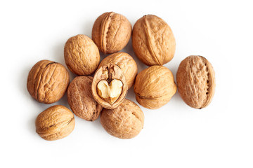 A pile of walnuts with one cracked half on the top which has a heart shaped kernel inside of it, top view, isolated on white background