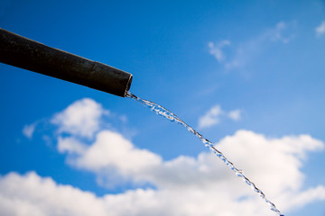 Drops of water flowing from pipe - close up with blue sky. Concept for water shortage and...