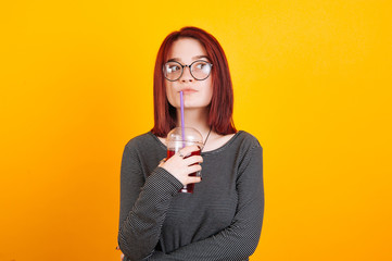 Red head young girl grinking red juice on yellow background wearing glasses.