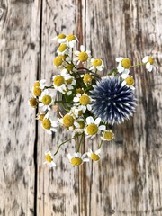 Chamomile and echinops bouquet in the vase on the old wood table. Wooden texture and vintage look.