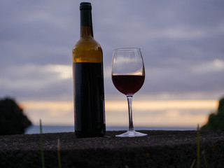 Wine bottle and glas with the sunset sky and sea in the background