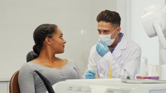 Attractive young African woman using her smart phone while visiting dentist. Professional dentist and his female patient smiling joyfully to the camera before dental checkup.