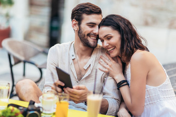 Young couple of tourist sitting in a cafe, drinking coffee and using tablet.
