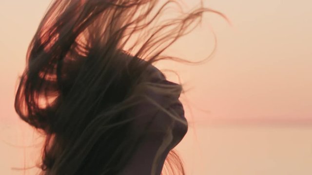 Slow motion teenage girl flipping hair on a beach at sunset