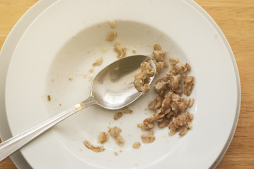 Empty dish of oat meal porridge breakfast in white plate dish with spoon. Eating breakfast morning. Wooden table. Close up healthy food. Top view.