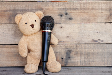 Teddy bear stand up with microphone for sing on wood background.