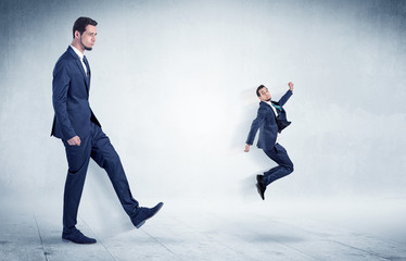 Big businessman kicking small businessman who is flying away with his briefcase on his hand
