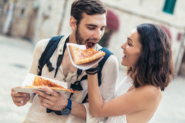 Happy couple of tourist eating pizza on street