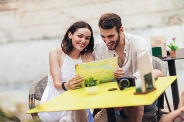 Young tourists having coffee at cafe and reading map