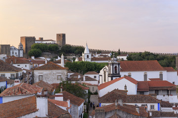 Scenic view of white houses red tiled roofs. and castle of Obidos from wall of fortress. Beautiful old town with medieval architecture in the sunset.