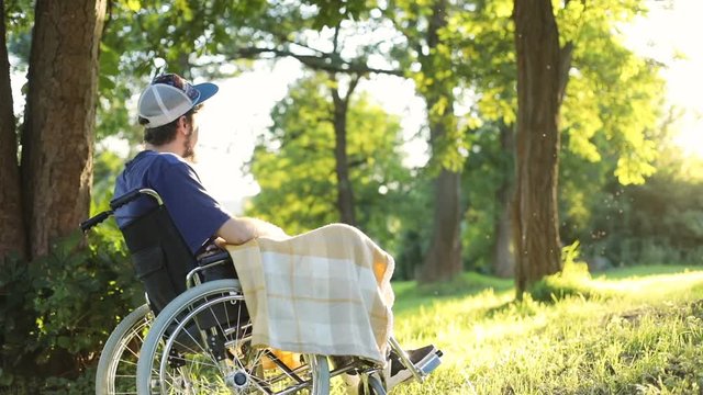 unidentified young man in a wheelchair enjoying fresh air and looking at sun setting over the horizon summer rest health care disease prevention physical recovery paralyzed body disability pension
