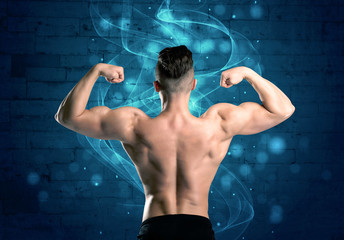 Fototapeta na wymiar A sexy body builder lifting weight and showing his muscular, hot body in front of a blue urban brick wall with drawn light beams concept