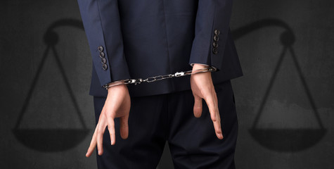 Fototapeta na wymiar Arrested businessman in handcuffs with hands behind back and justice symbol wallpaper 