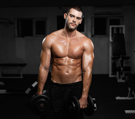 Fototapeta na wymiar Muscular male athlete posing with dumbbells in the gym