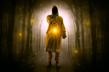 Man in raincoat coming from dark forest with glowing lantern in his hand concept
