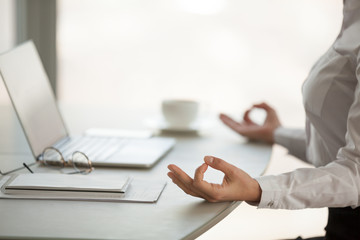 Close up of calm worker meditating in lotus position in office, female employee practicing yoga at...