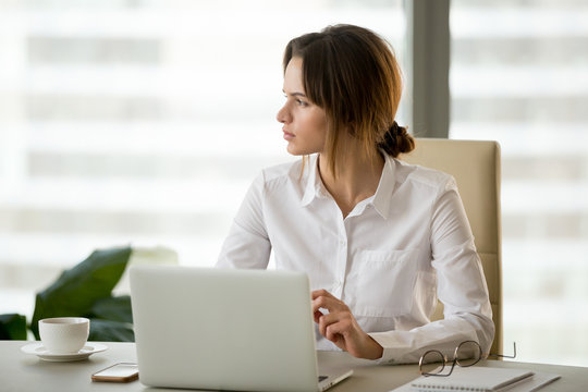 Serious businesswoman sitting at office desk looking away thinking about business problem solution, thoughtful female boss considering new project implementation, planning future successful startup