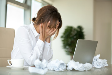 Stressed female worker feel despair surrounded by crumpled paper not able to write business letter...