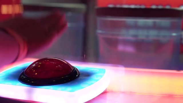 4K shot of a hand rapidly smashing the big red button on an arcade game.
