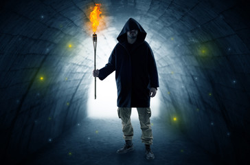 Ugly man with burning flambeau walking in a dark tunnel