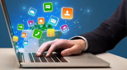 Businessman hand typing on laptop with flying application icons around
