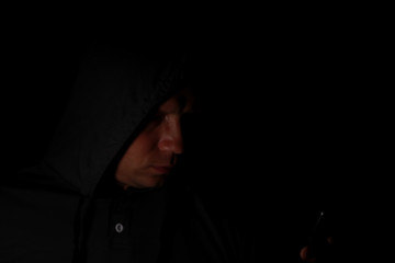 The man's portrait in a hood with the mobile phone in the dark.
