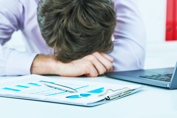 Tired overworked young businessman sleeping over a laptop in a desk at job in his office.