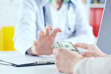 Female doctorpulls a hand for bunch of hundred dollars banknotes. Concept of corruption in the medical industr - 216395223