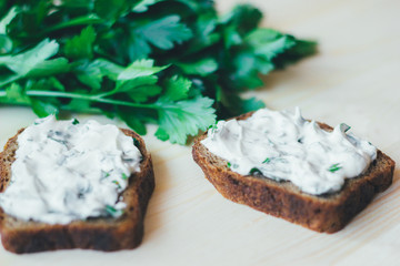 Toasts from greens and sour cream on a wooden background. Green branches of fresh parsley behind.