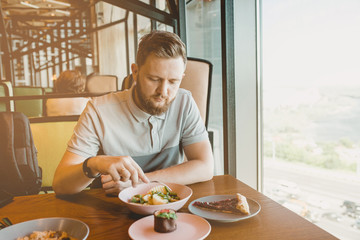 a man with a beard sitting at the table cafe and eating beans with potatoes, cakes next