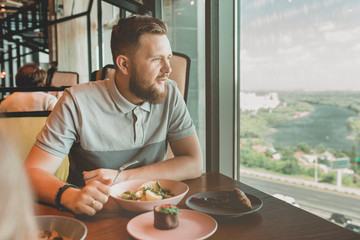 a man with a beard sitting at the table cafe and eating beans with potatoes, cakes next