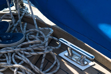 Close-up of a rope with a knotted end tied around a cleat on a wooden pier and shoes with anchors