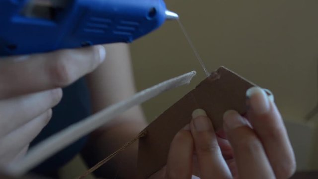 A women making miniatures with papper board and painting in a white canvas de picture of a man with crayolas, brushes, pens, crayons, water colors. Close to a window, daylight.