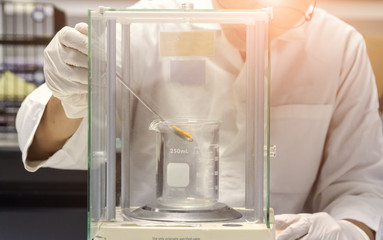 close up of hand wear glove is pouring sample to beaker to weighting on electronic balance in chemical laboratory
